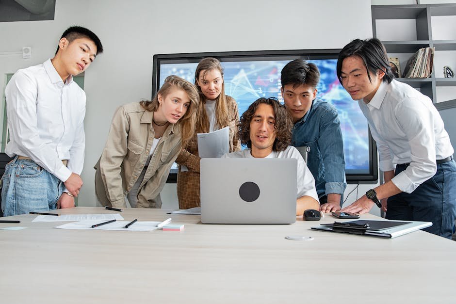 A diverse group of young professionals brainstorming during a collaborative meeting around a laptop in an office.